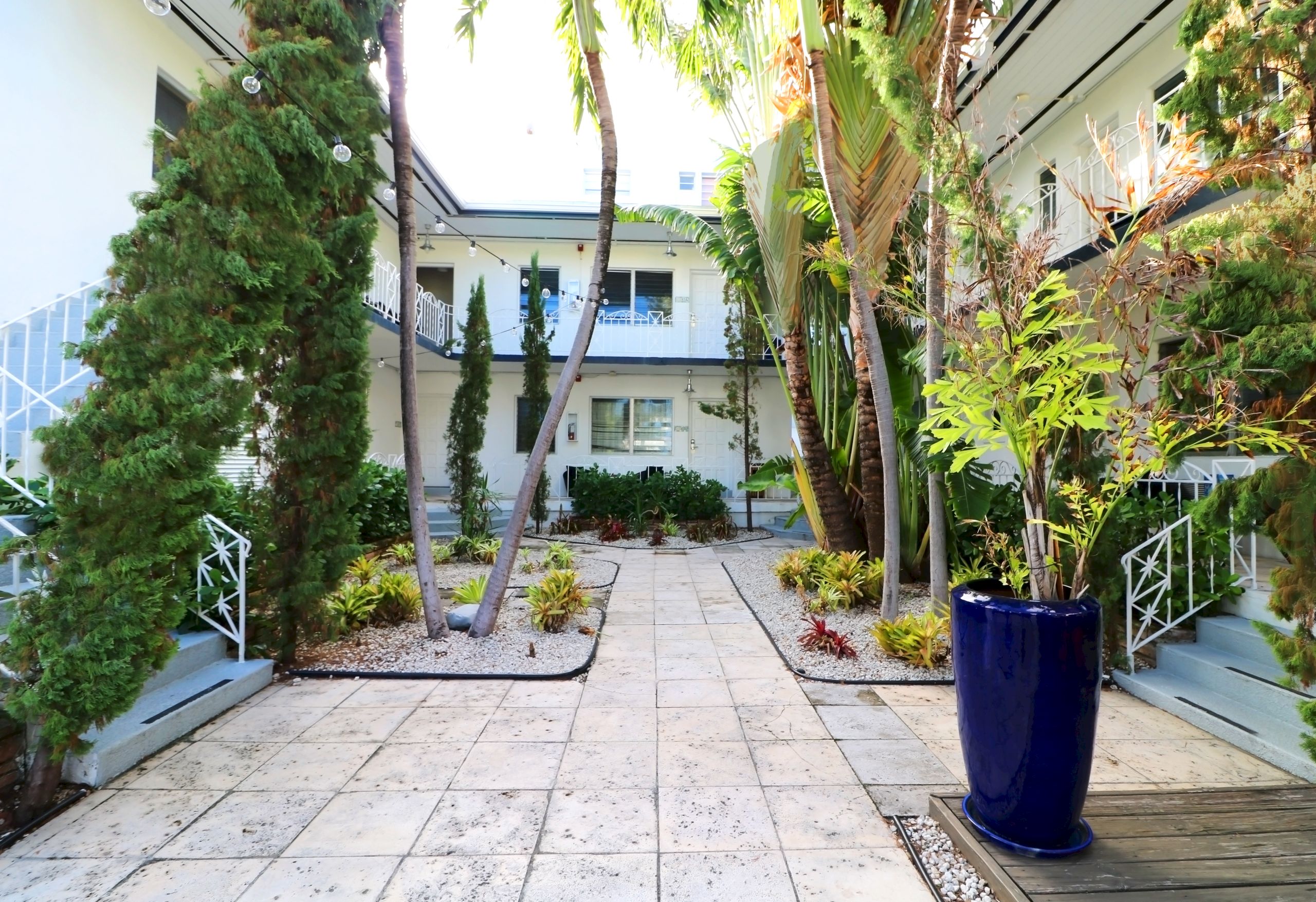 A courtyard with a tiled walkway, plants, and trees.