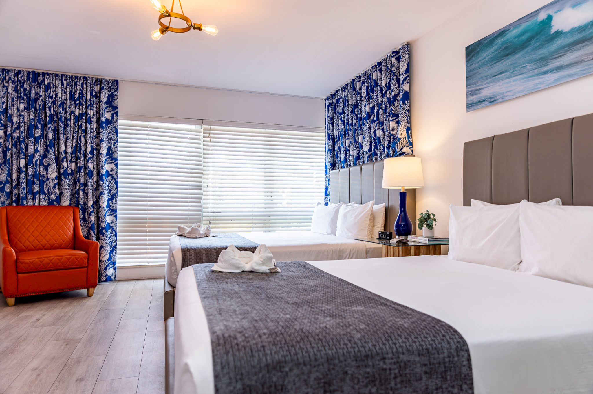 A hotel room with two beds, an orange chair, and blue curtains.