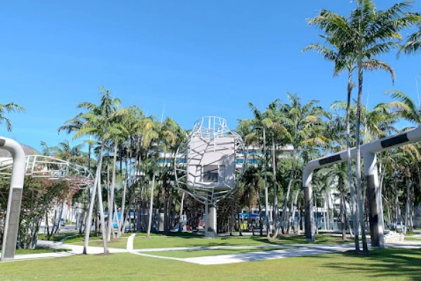 A large outdoor space with palm trees, a grassy area, and a modern sculpture in front of a building.