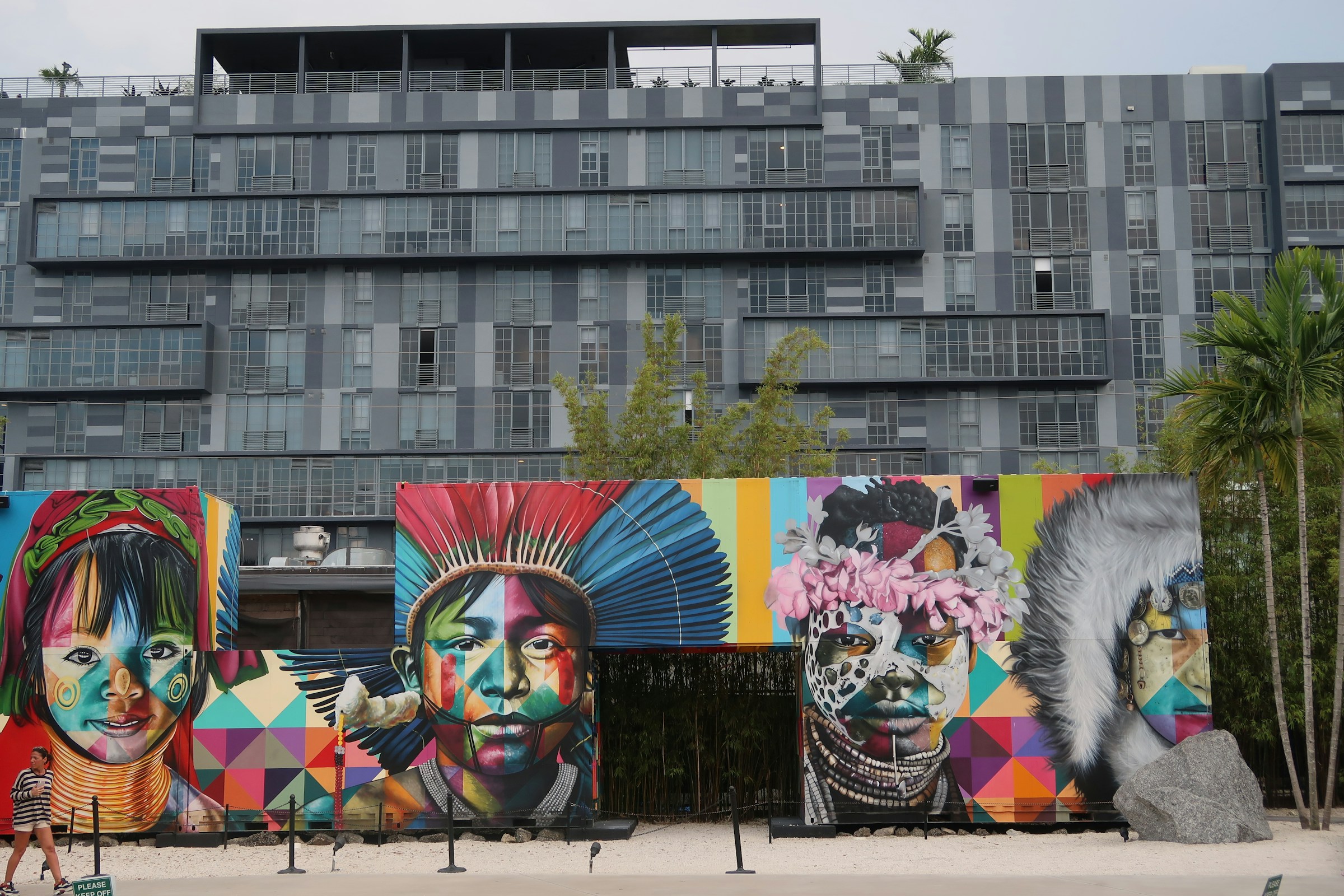 A large building with a colorful mural on the side, located on a beach with palm trees.